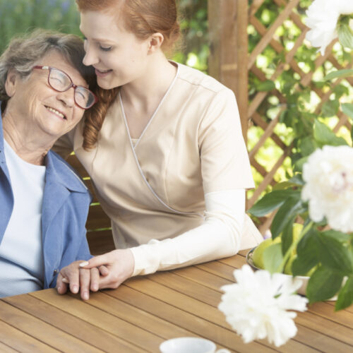 Happy grandmother enjoying time with friendly nurse on the terrace of sanatorium